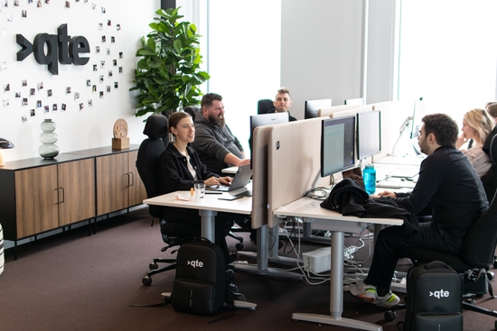 En grupp kollegor sitter vid sina skrivbord och ler på qte-kontoret.